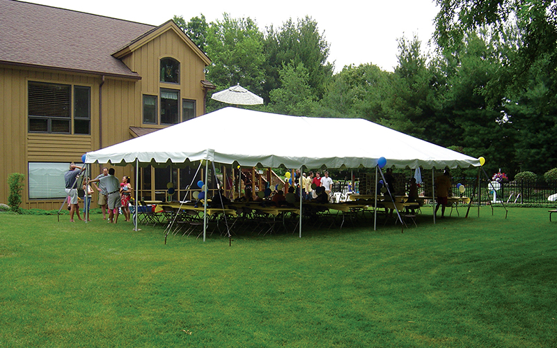 Family members celebrating together under a large white event tent in a backyard