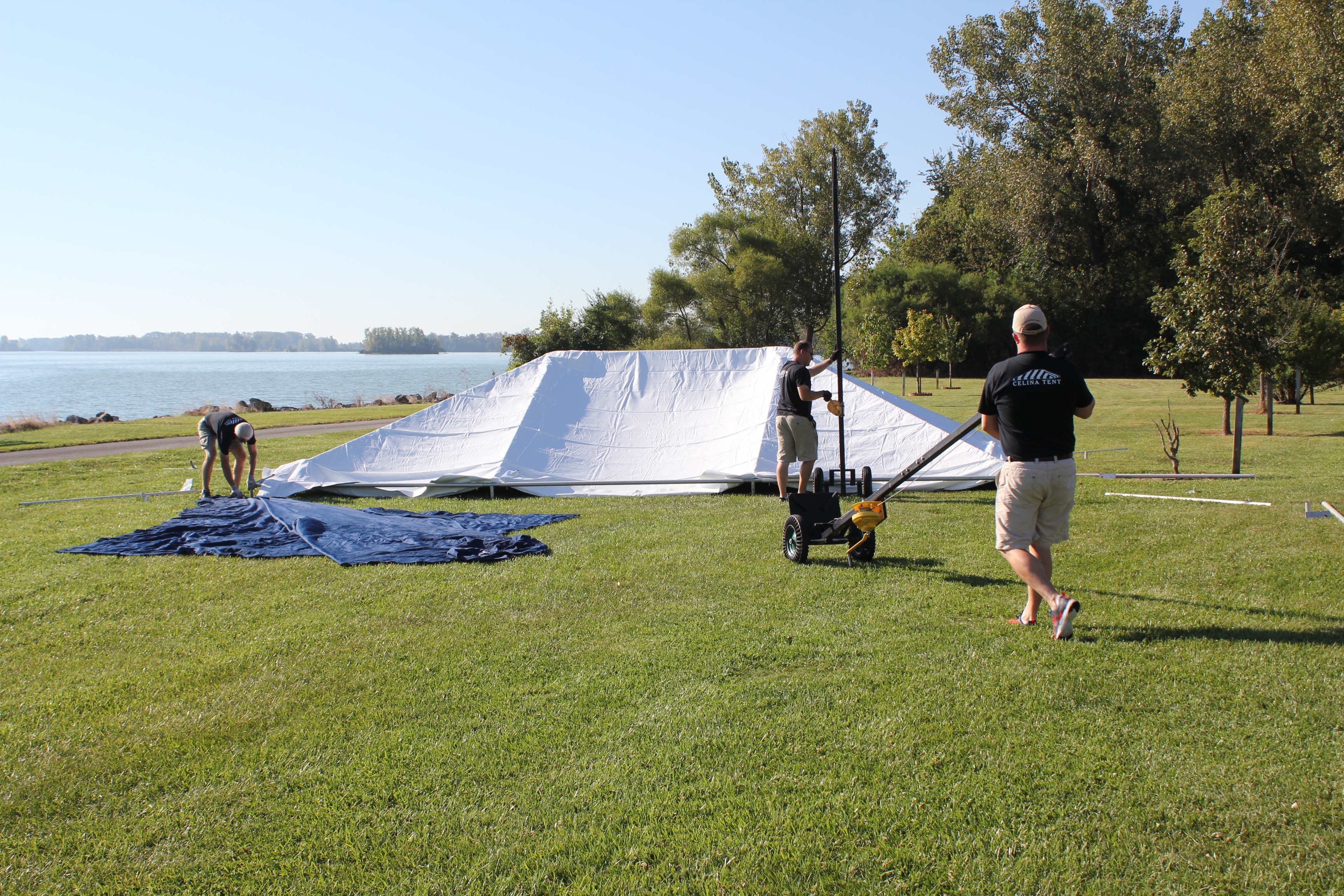 White event tent being setup by workers using installation tools and drop cloth