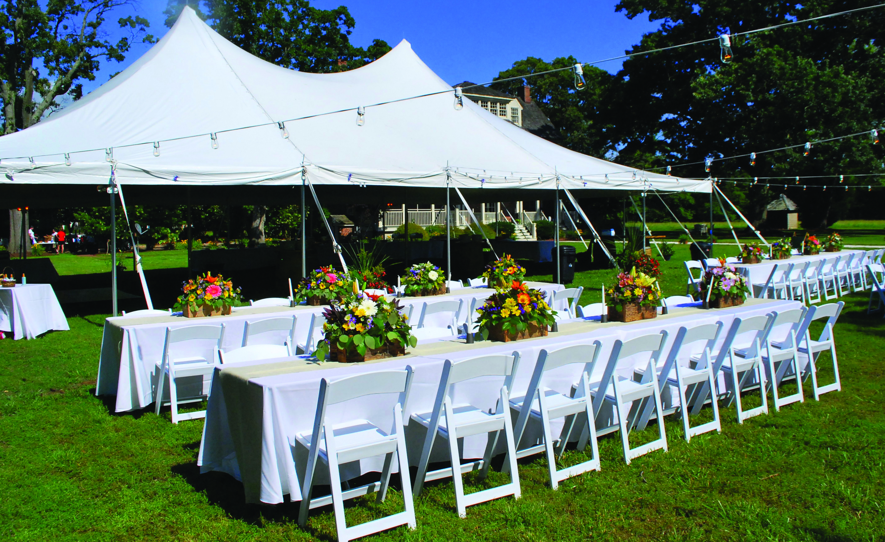 Premiere High Peak Pole Tent with resin garden chairs and banquet tables decorated with floral centerpieces for an outdoor event